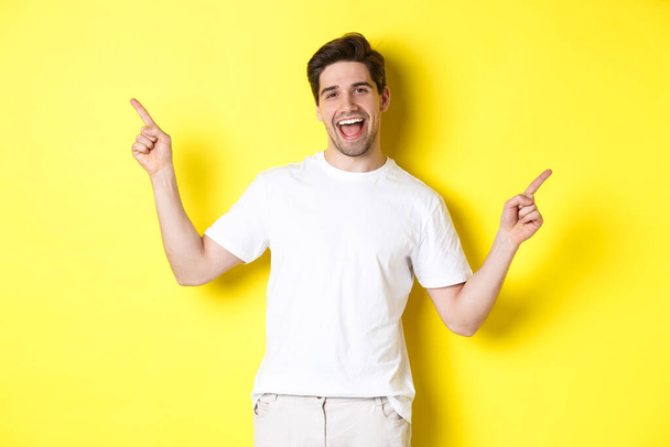 Happy stylish guy showing two variants, pointing fingers sideways at left and right promo, standing over yellow background - Foto, immagini