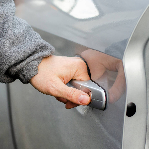 The hand of a man in warm clothes opens the door of the silver-colored car - Photo, image