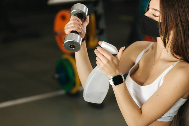 Sportswoman wearing protective face mask disinfecting her hands and dumbbells at the gym - Photo, image