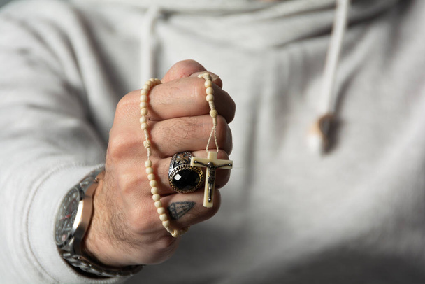 Un hombre con una mano tatuada sosteniendo un rosario - Foto, imagen