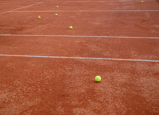 Mnoho míčků pro tenis ležící na červeném tenisovém kurtu - Fotografie, Obrázek