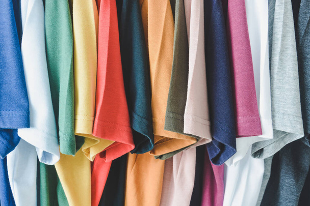 Nahaufnahme Sammlung bunter T-Shirts, die an Kleiderbügeln im Kleiderschrank oder Kleiderständer hängen - Foto, Bild