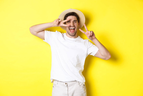Concept de tourisme et de vacances. Homme heureux touriste posant pour la photo avec des signes de paix, souriant excité, debout sur fond jaune - Photo, image