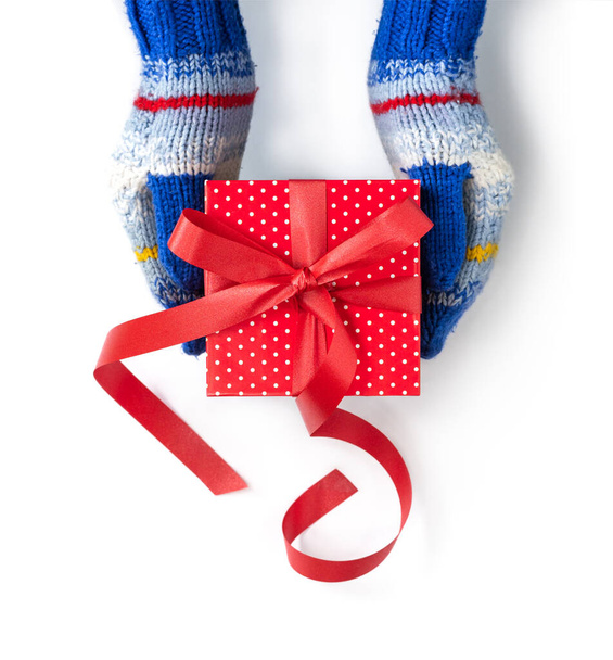 Mãos em mitenes listradas azuis está segurando um presente de Natal vermelho isolado no branco. - Foto, Imagem