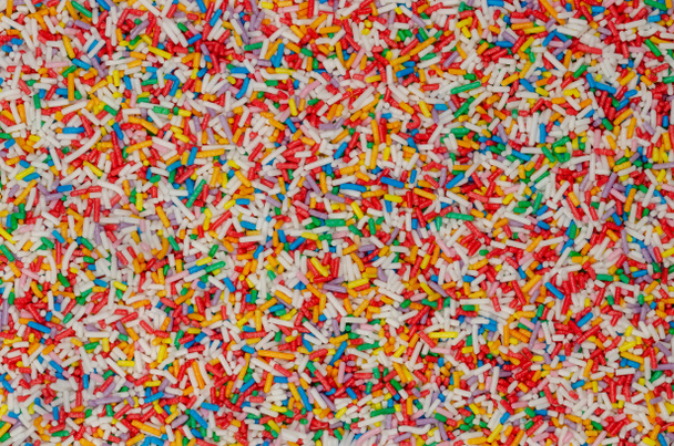 Regenboog hagelslag, achtergrond en oppervlak. Staafvormige kleurrijke suikerhagelslag. Kleine snoepjes in een verscheidenheid van kleuren, gebruikt als decoratie of topping. Achtergrondinformatie. Voedsel foto, bovenaanzicht, van boven. - Foto, afbeelding