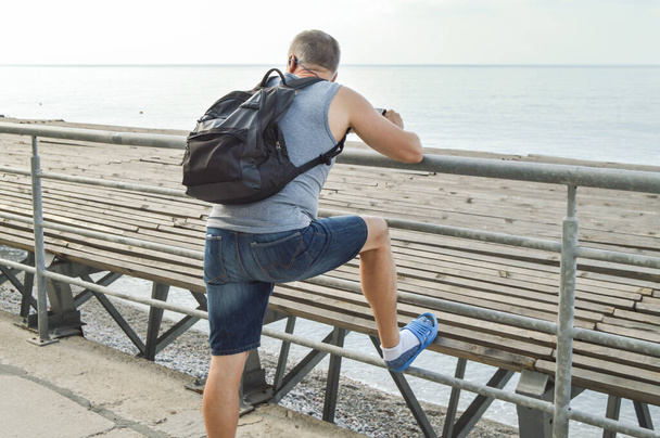 Voyageur homme avec un sac à dos relaxant en pleine mer, regardant l'aube, appuyé sur le parapet, le concept d'un mode de vie de liberté et de détente. - Photo, image