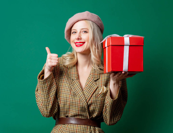 Mujer rubia en chaqueta de estilo británico con caja de regalo sobre fondo verde - Foto, Imagen