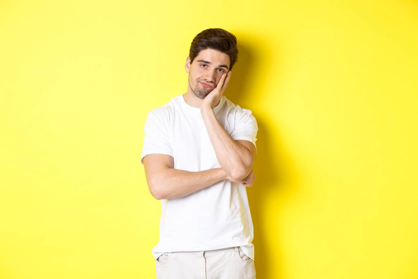 Znudzony i niezadowolony człowiek patrzący z obojętnością, stojący w białych ubraniach na żółtym tle - Zdjęcie, obraz