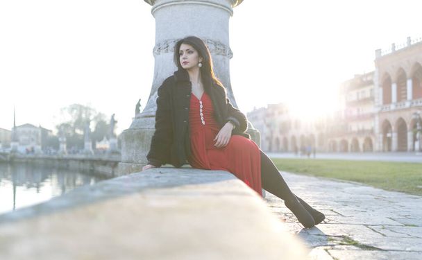 menina bonita com cabelo preto longo ao pôr do sol sentado na praça em Pádua. Foto de alta qualidade - Foto, Imagem