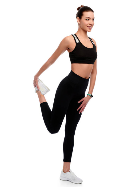 Тонкая атлетичная белая женщина в спортивной одежде делает упражнения на растяжку на белом изолированном фоне - Фото, изображение