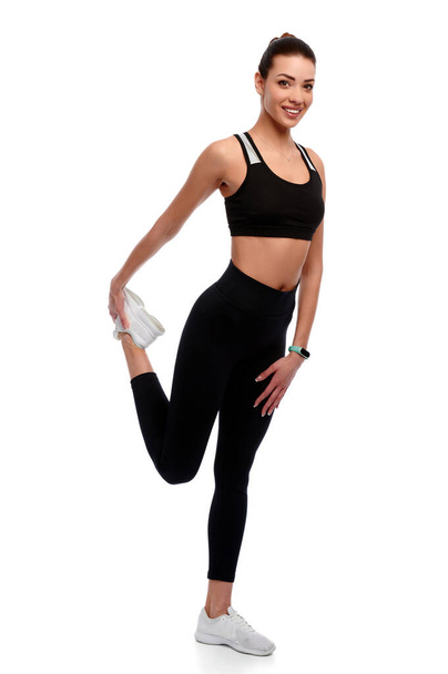 Стройная сильная атлетичная женщина в спортивной одежде делает упражнения на растяжку на белом изолированном фоне - Фото, изображение