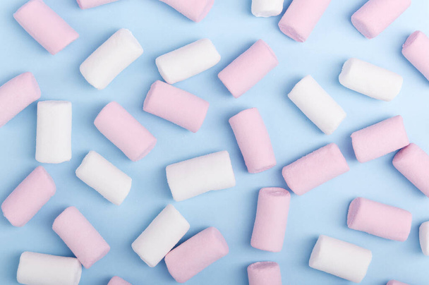 Egy csomó fehér és rózsaszín mályvacukor pasztell fényű háttérrel. Színes egészségtelen édességek felülről. Kék textúra háttér cukorka felső nézet. - Fotó, kép