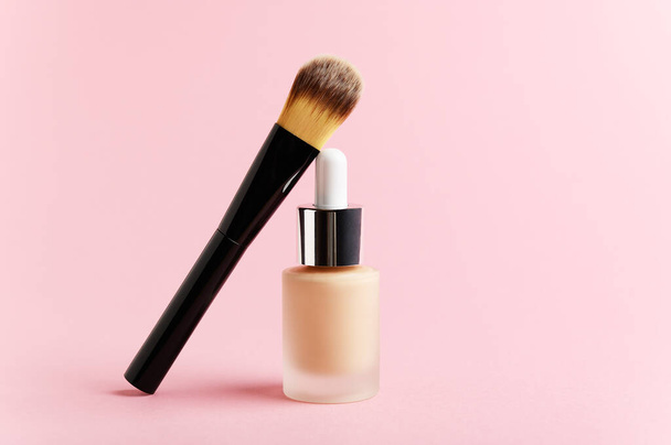 Liquid foundation cream unbranded bottle with makeup brush. Facial correction, liquid concealer, tone, bb, cc cream skincare product on pink background. Feminine cosmetics accessory with copy space. - Photo, Image