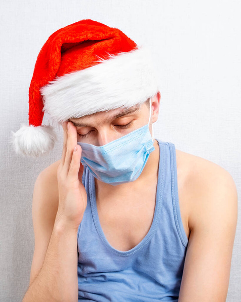 Sad Young Man in Santa Hat and Flu Mask by the Wall in the Room - Foto, immagini