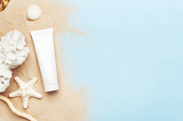 Tube with hand cream, body lotion or sunscreen. Summer decoration as starfish, seashell and sand on blue background. Mockup style. Copy space in right side. Wellness and beauty concept. - Foto, Imagen