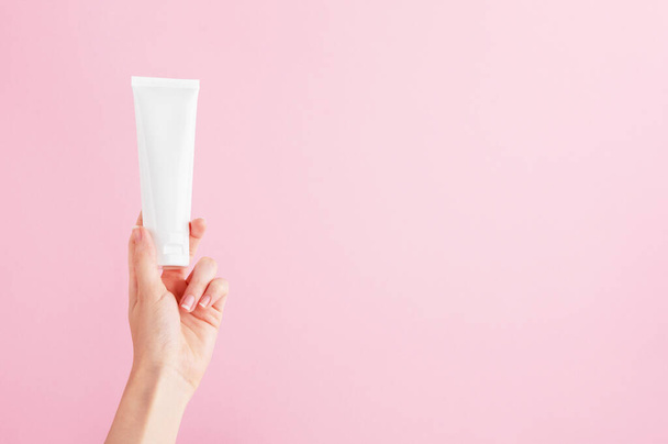 Unbranded flacon for cream, concealer, toiletry. Plastic tube in female hand. Container for professional cosmetics products. Skincare and beauty concept. Mockup, copy space. Isolated on pink. - Photo, Image