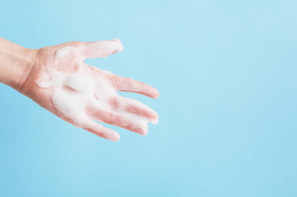 Osoby ręka w żel pod prysznic lub bańki mydlane izolowane na niebieskim tle. Antybakteryjne mycie rąk. Koncepcja higieny osobistej i zdrowia. Przestrzeń kopiowania po prawej stronie. - Zdjęcie, obraz
