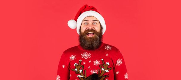 brutal bearded man in santa claus hat. happy new year. merry christmas. mature hipster wear knitted sweater. xmas shopping sales. man with beard on red background - Foto, imagen