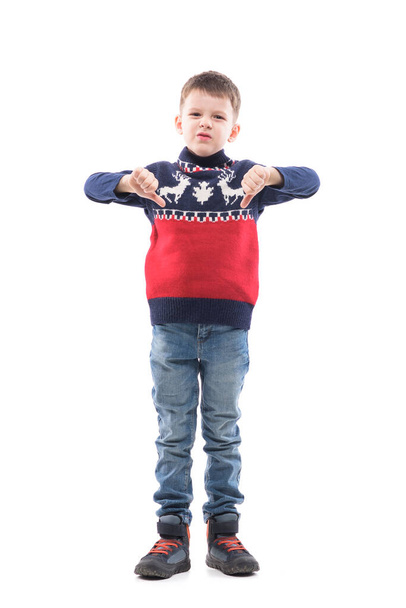 Cute displeased young boy in Christmas sweater showing thumbs down gesture frowning at camera. Full body portrait isolated on white background.  - Foto, imagen
