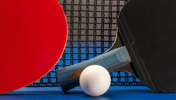 Дві настільні тенісні ракетки та м'ячі на синьому столі з сіткою
. - Фото, зображення