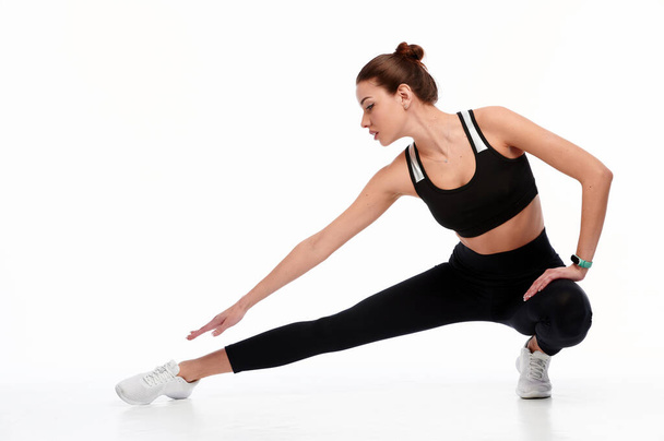glimlachende sport vrouw stretching benen terwijl geïsoleerd op een witte achtergrond - Foto, afbeelding