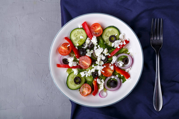 Light plate of Greek salad on a blue napkin on a concrete background. - Φωτογραφία, εικόνα