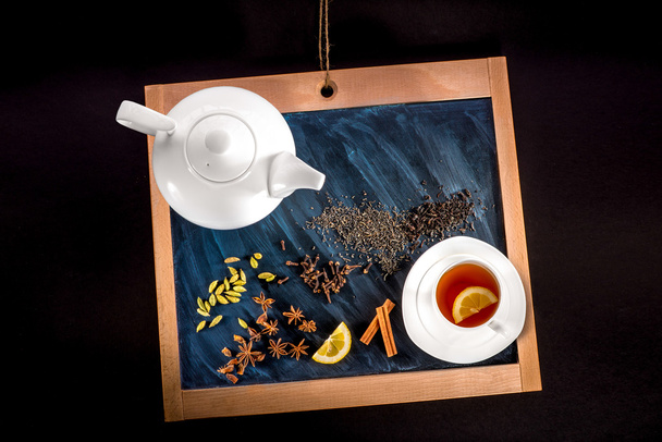cup of tea and teapot with spices and lemon on chalkboard on bla - Photo, Image