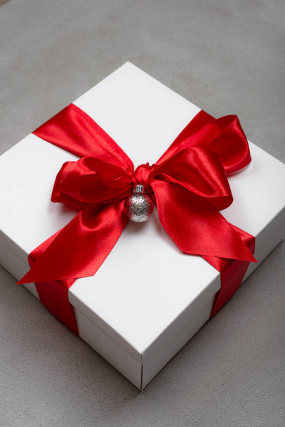 White christmas gift box with red ribbon on gray background - Photo, Image