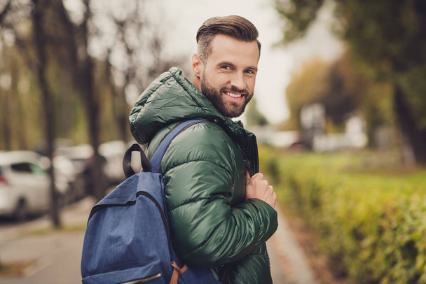 Photo of satisfied bearded person turn head to camera toothy smile good vibes carry blue bag walking outdoors - Foto, afbeelding