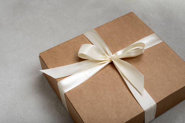Craft colored christmas gift box with white ribbon on gray background - Fotografie, Obrázek