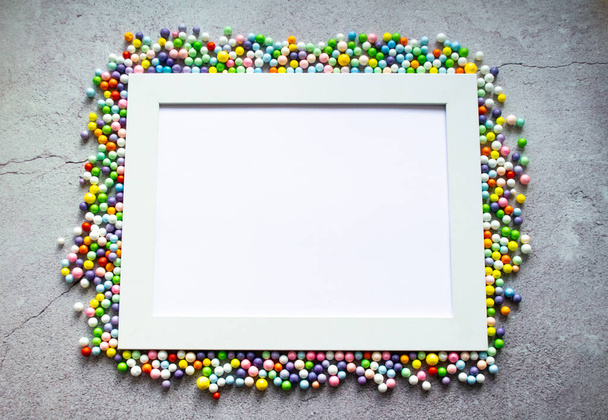 White frame with multicolored small balls around. Against the background of cracked concrete. Copy space. - Foto, Bild
