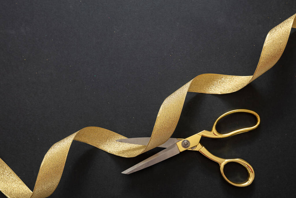Grande inauguração. Tesoura de ouro cortando fita de seda dourada, fundo preto, vista superior. Modelo de convite, espaço de cópia - Foto, Imagem