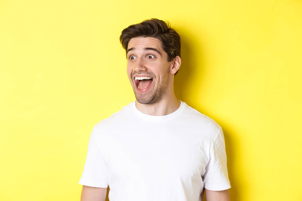 Kép boldog ember nézi promo, nézett balra csodálkozva, álló fehér póló sárga háttér - Fotó, kép