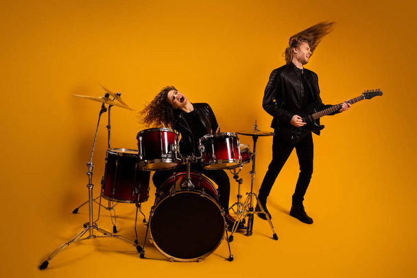 Full body photo of rock group cool guy play guitar crazy girl beat drum sticks popular song excited concert show hairdo flight wear black leather outfit isolated yellow background - Фото, зображення