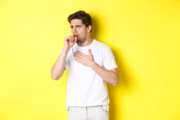 Image of man with covid-19 or flu symptoms, coughing and feeling sick, standing over yellow background - Фото, изображение