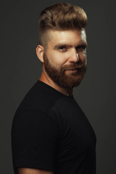 Fabulous at any age. Portrait of smiling 35-year-old man with fit body standing over gray background in black t-shirt. Hipster style. Red hair, modern haircut. Studio shot - Foto, Imagen
