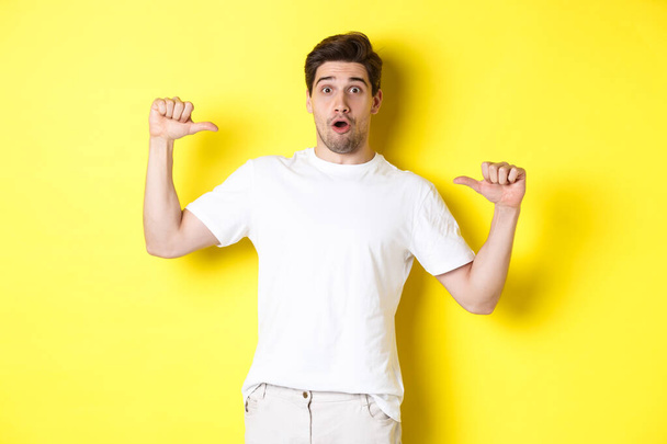 Surprised handsome guy pointing at himself, looking amazed, standing over yellow background - Fotografie, Obrázek