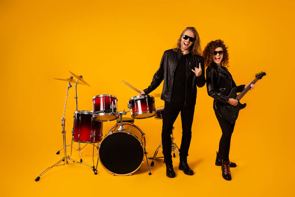 Full length photo popular funky two people punk artist enjoy performance concert girl play bass guitar man hold drumstick show horns symbol wear leather jacket isolated bright color background - Fotografie, Obrázek