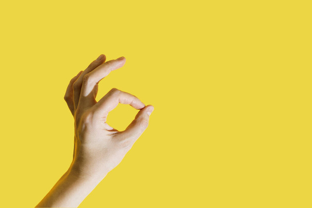 Female hand folded into a symbol okay on a bright yellow illuminating background. Trendy color of the year 2021. - Foto, afbeelding