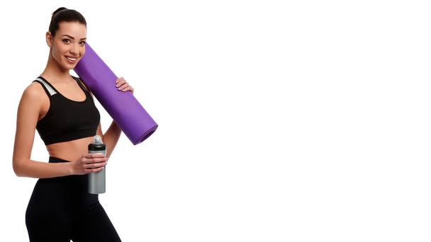 Blanke sterke vrouw met mat en fles water op witte geïsoleerde achtergrond. Fitness Instructeur draagt sportkleding. Begrip gezondheidszorg en gewichtsverlies - Foto, afbeelding