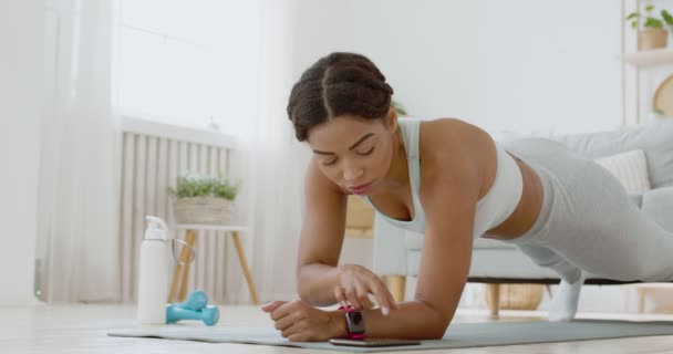 Giovane signora accendere cronometro sul suo fitness tracker, praticare allenamento tavola a casa - Filmati, video