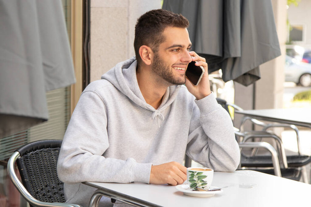 jeune homme barbu parlant sur téléphone portable à la table de terrasse café - Photo, image
