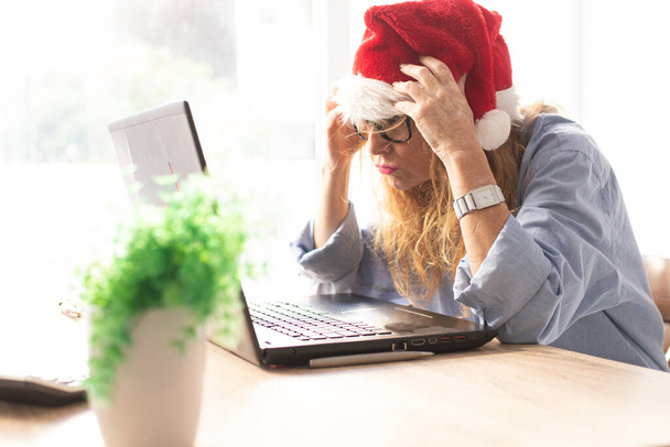donna con cappello da Babbo Natale e computer con espressione di stanchezza o sopraffazione - Foto, immagini
