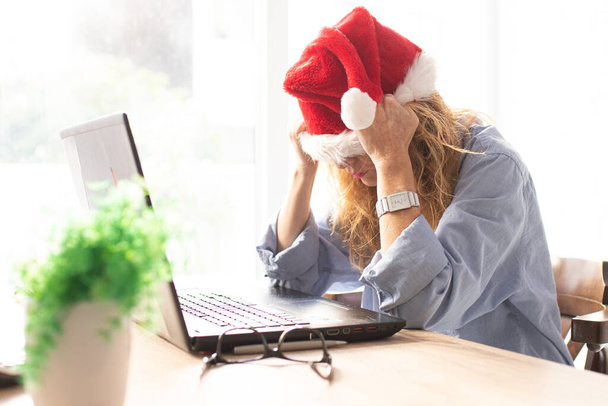 kobieta z kapeluszem i komputerem Świętego Mikołaja z wyrazem zmęczenia lub przytłoczenia - Zdjęcie, obraz