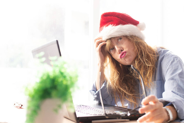 žena s kloboukem Santa Claus a počítačem s výrazem únavy nebo ohromení - Fotografie, Obrázek