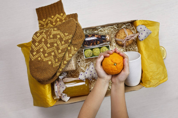 Cute girl packing festive care box with tea, honey, cookies and knitted wool socks for grandmother. Personalized care box during lockdown, support and surprise for family and friends on Christmas - Photo, Image
