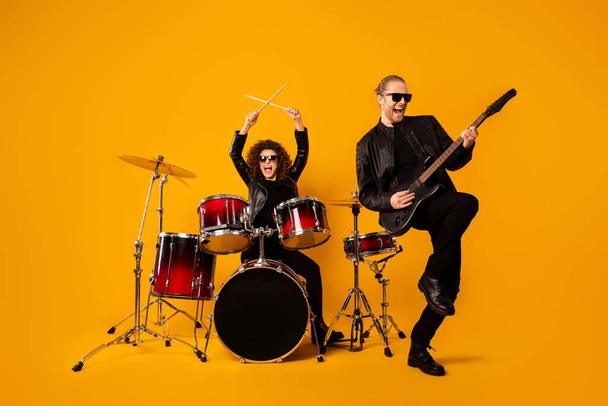 Full body photo of popular rock group guy play electric guitar pretty girl sit drum instruments beat night club performance concert hall wear black leather clothes isolated yellow background - Foto, Bild