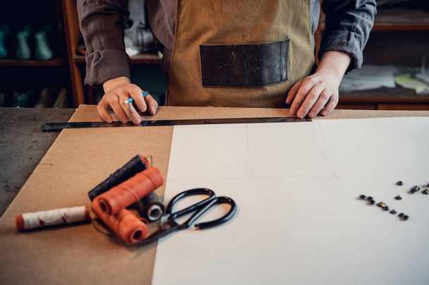 Ручное изготовление обуви в мастерской сапожник начинает с подготовки рисунка из бумаги на столе - Фото, изображение