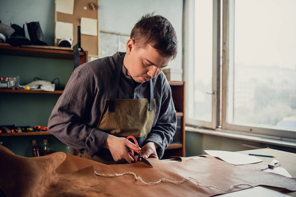 Un jeune tanneur dans son atelier à la table découpe des éléments en cuir de chaussures - Photo, image