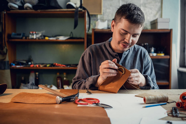 A young shoemaker manually sews decorative elements to leather shoes in the workshop - Photo, Image